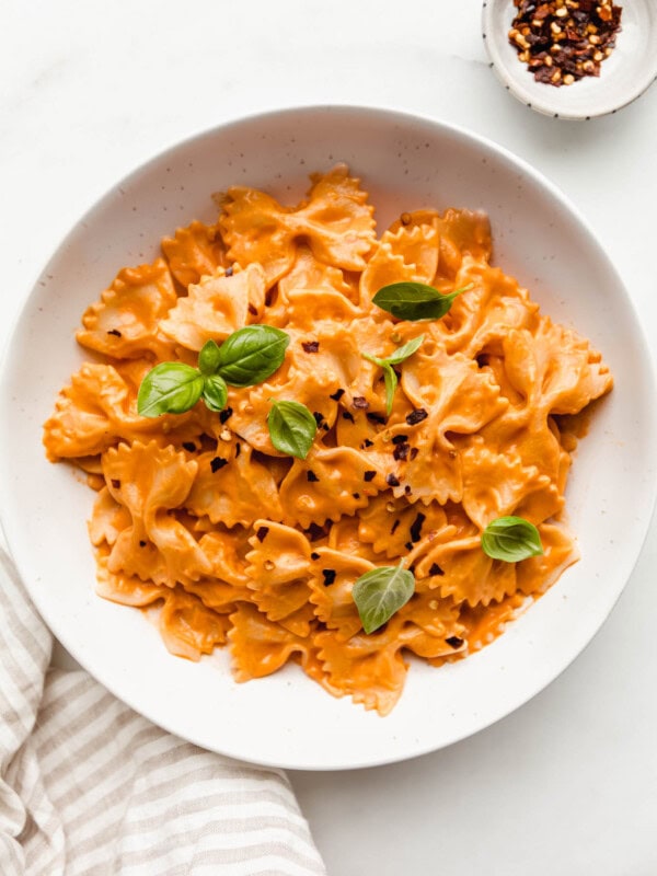 A bowl of vegan vodka pasta with a side of chili flakes and a napkin