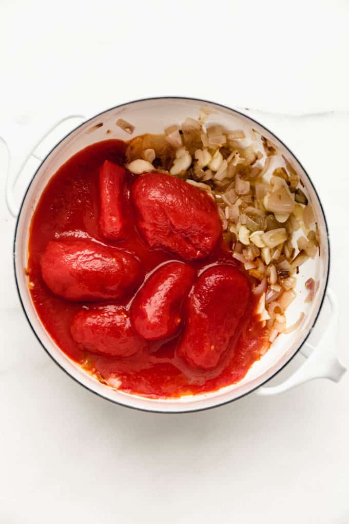 A white pot with canned tomatoes, garlic and shallots in it