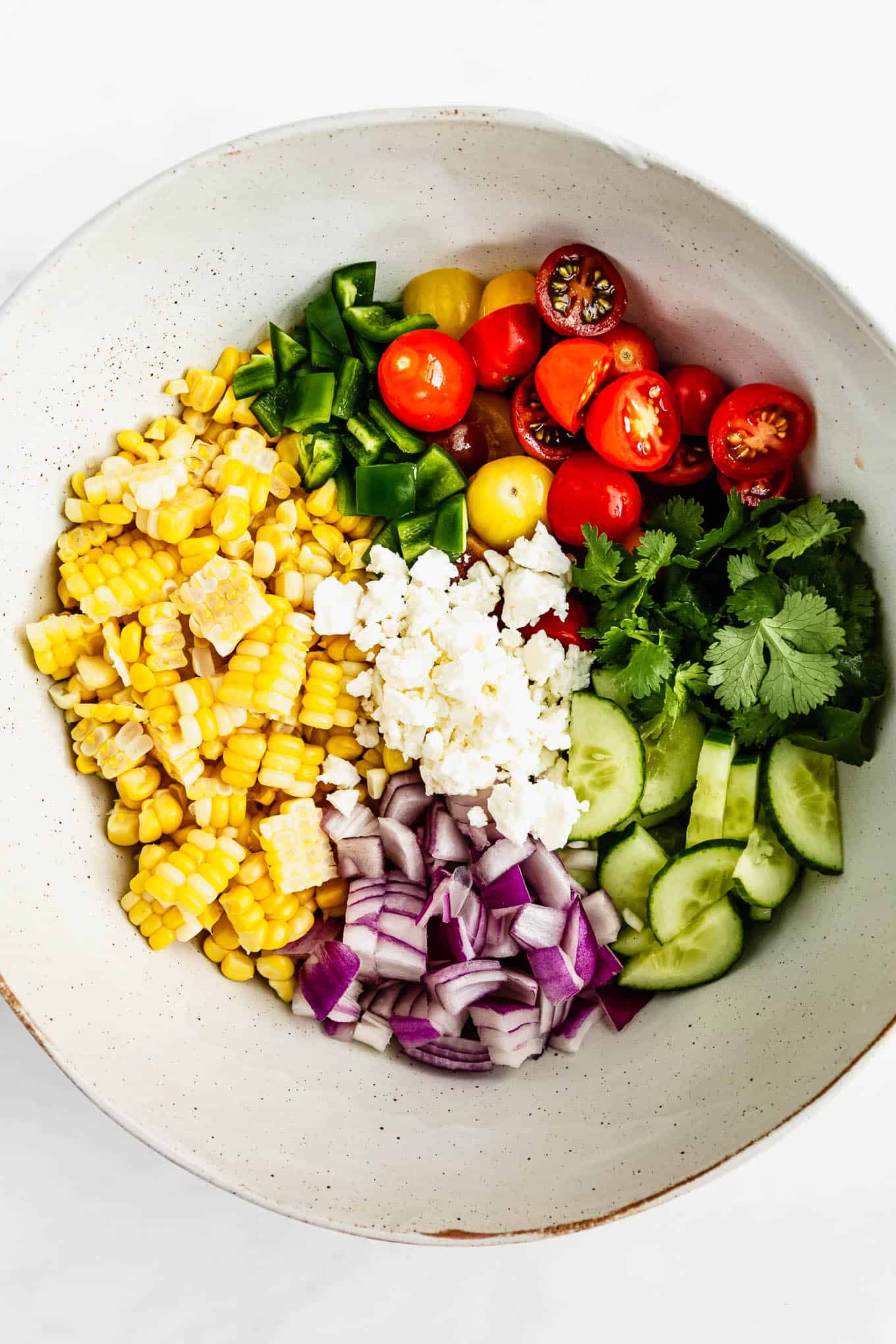 A bowl with corn, tomatoes, onion, cucumber, herbs and feta in it