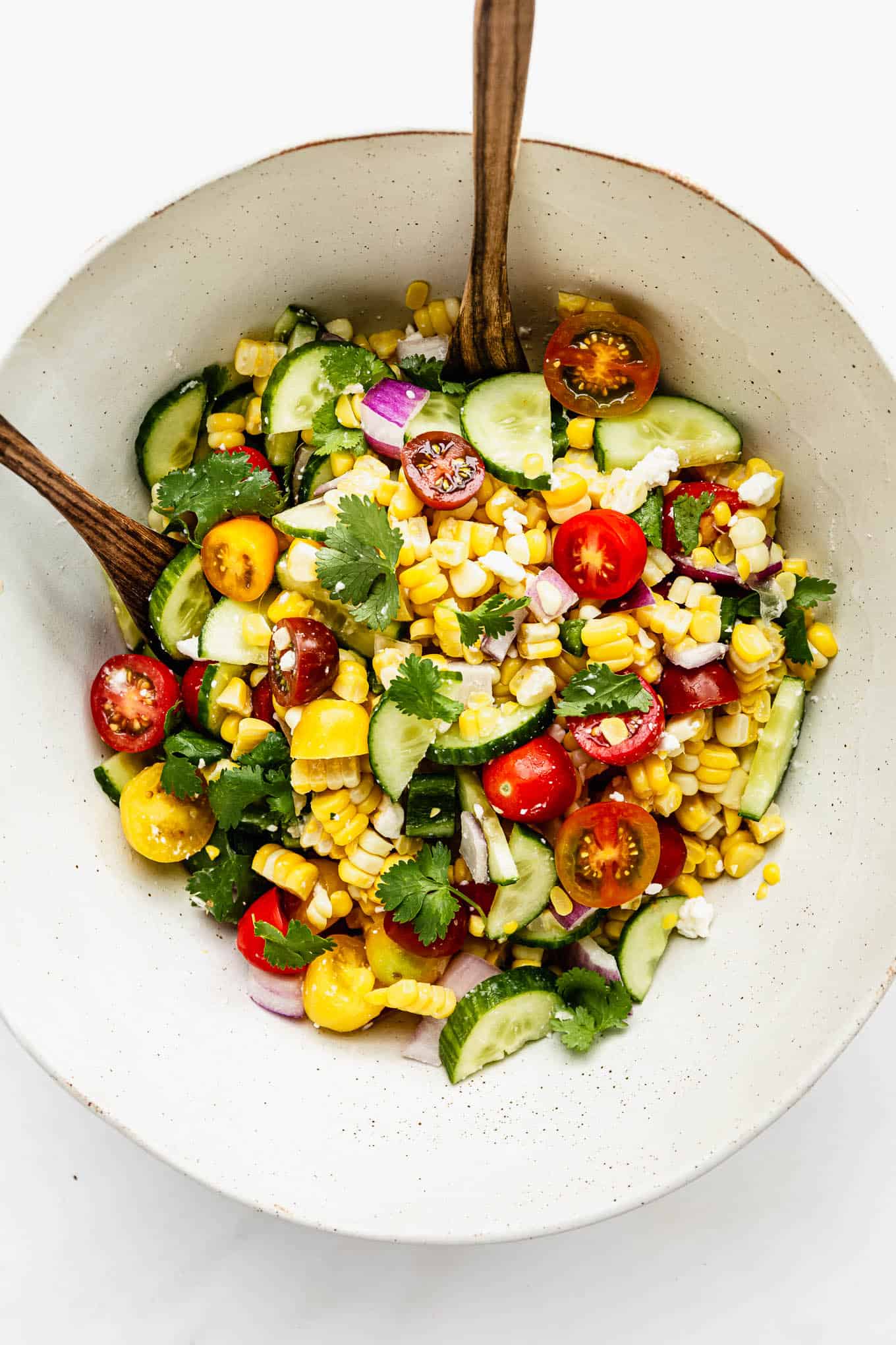 Summer corn salad in a large mixing bowl with wood spoons