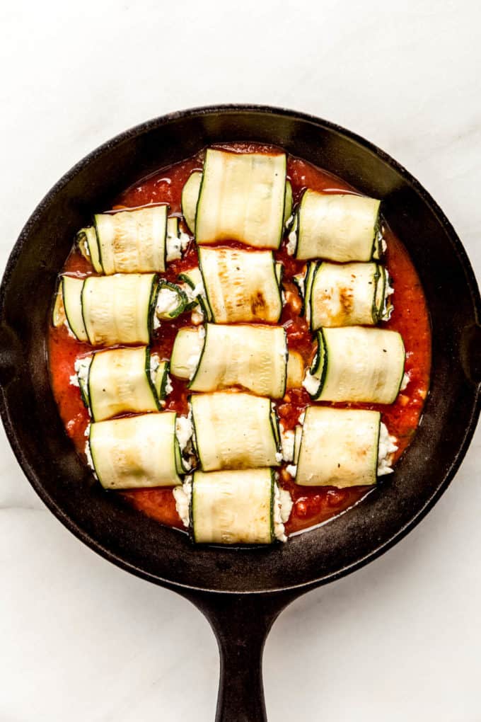 zucchini roll ups on tomato sauce in a cast iron skillet