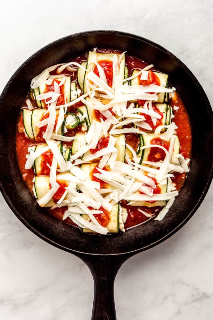 Zucchini roll ups topped with shredded cheese in a cast iron skillet