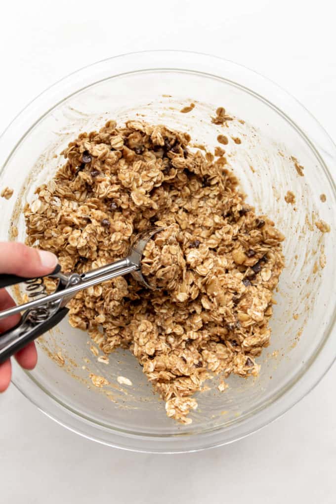 a hand using a cookie scoop to scoop batter out of a mixing bowl