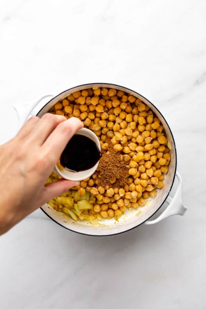 A hand pouring tamari into a pot of chickpeas