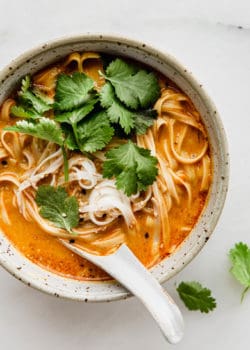A bowl of Thai Coconut Soup with noodles and a soup spoon in it