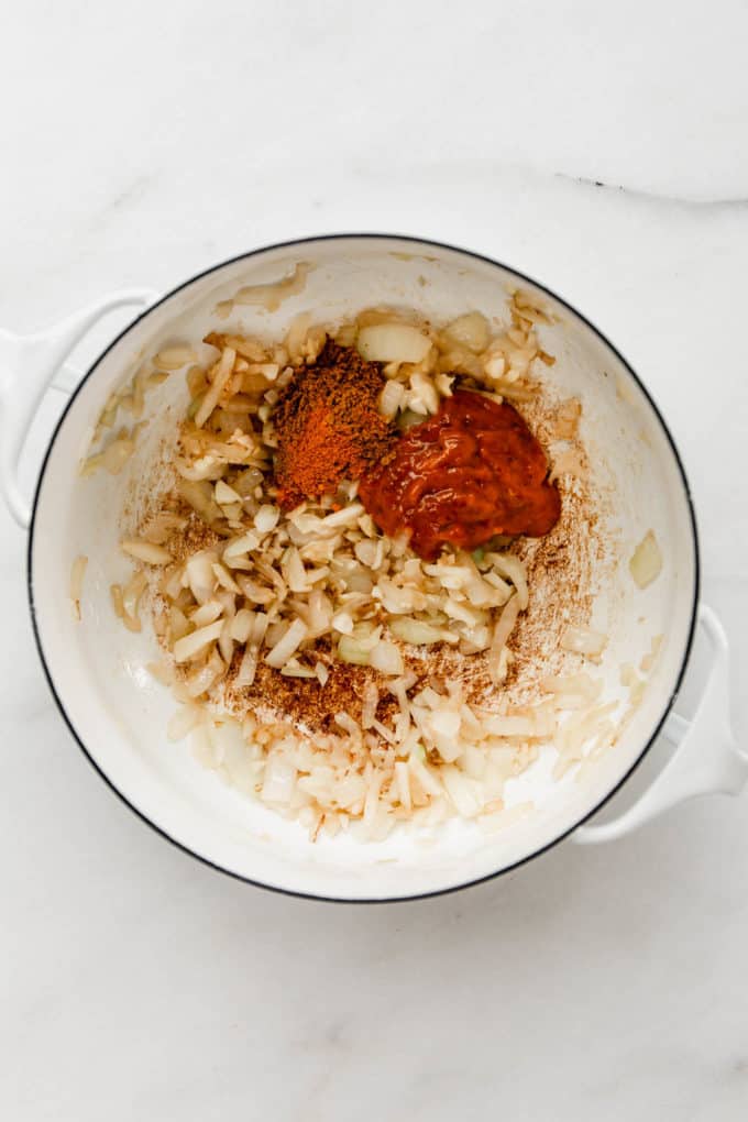 A white pot with onions, garlic, ginger, curry paste and spices in it