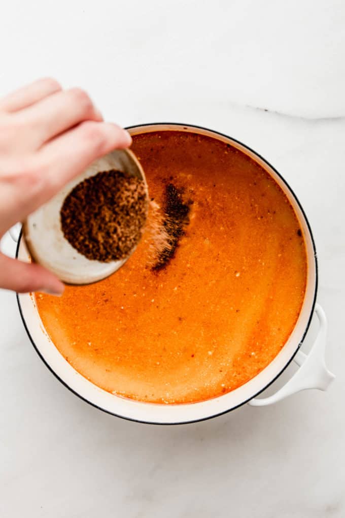 A hand pouring coconut sugar into a white pot of Thai coconut soup