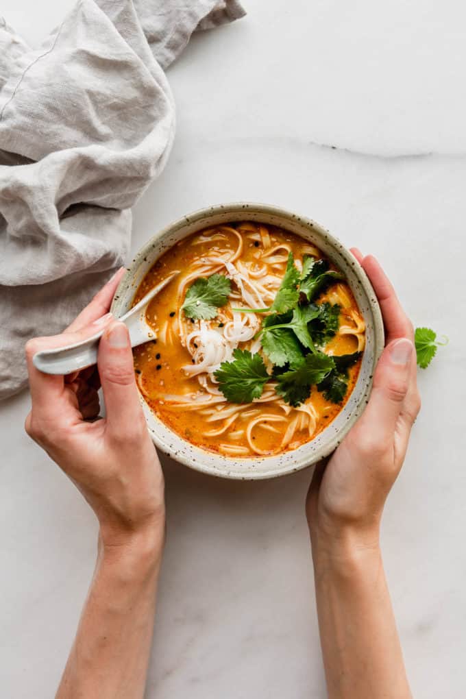 A hand holding a soup spoon in a bowl of Thai coconut soup