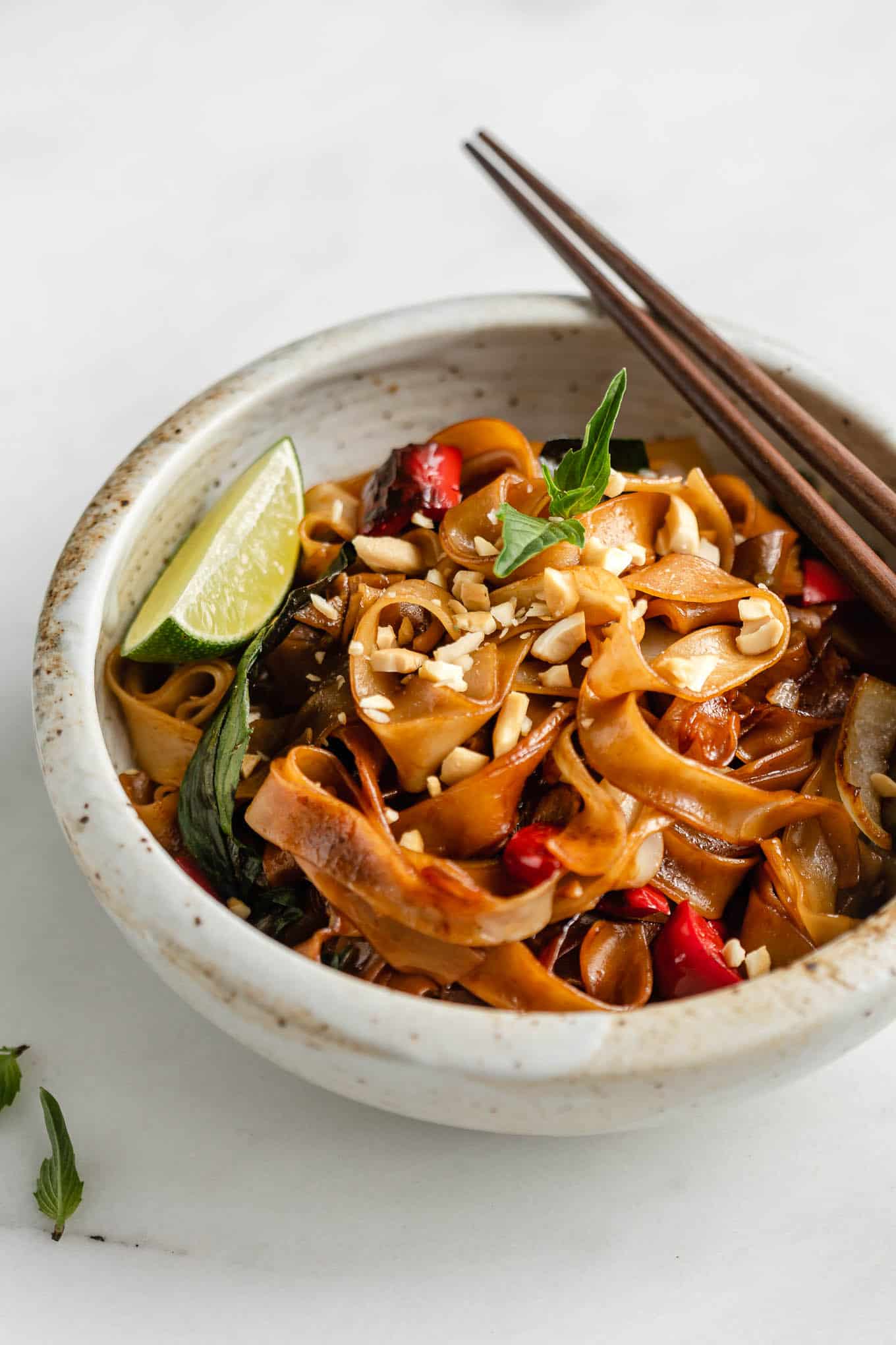 A bowl of Thai drunken noodles topped with crushed peanuts and a lime wedge