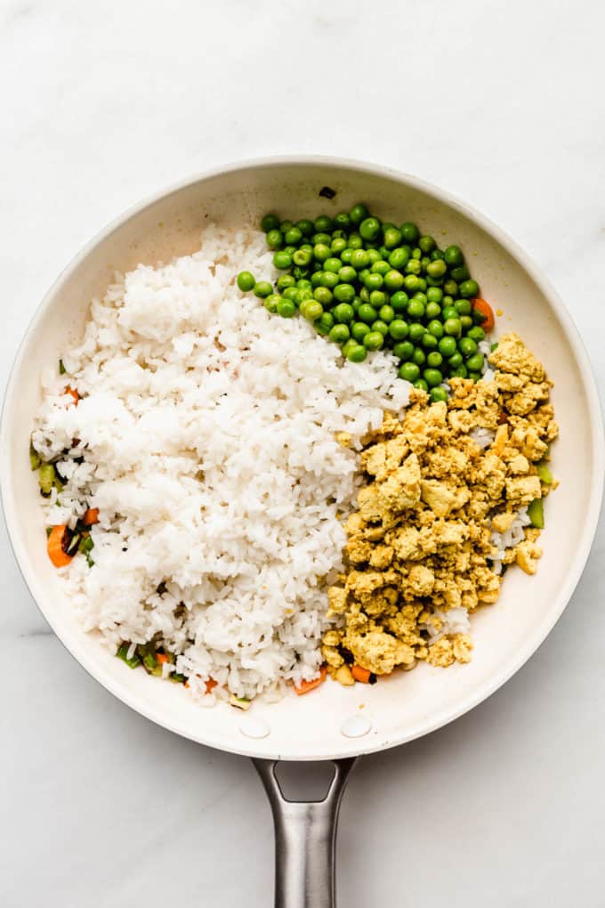 A white pan with rice, scrambled tofu and peas in it