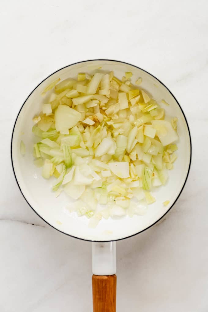 A white pot with onions and garlic in it