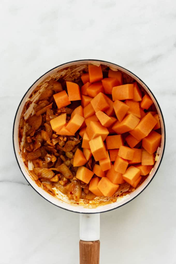 A white pot with cubed butternut squash and onions in it