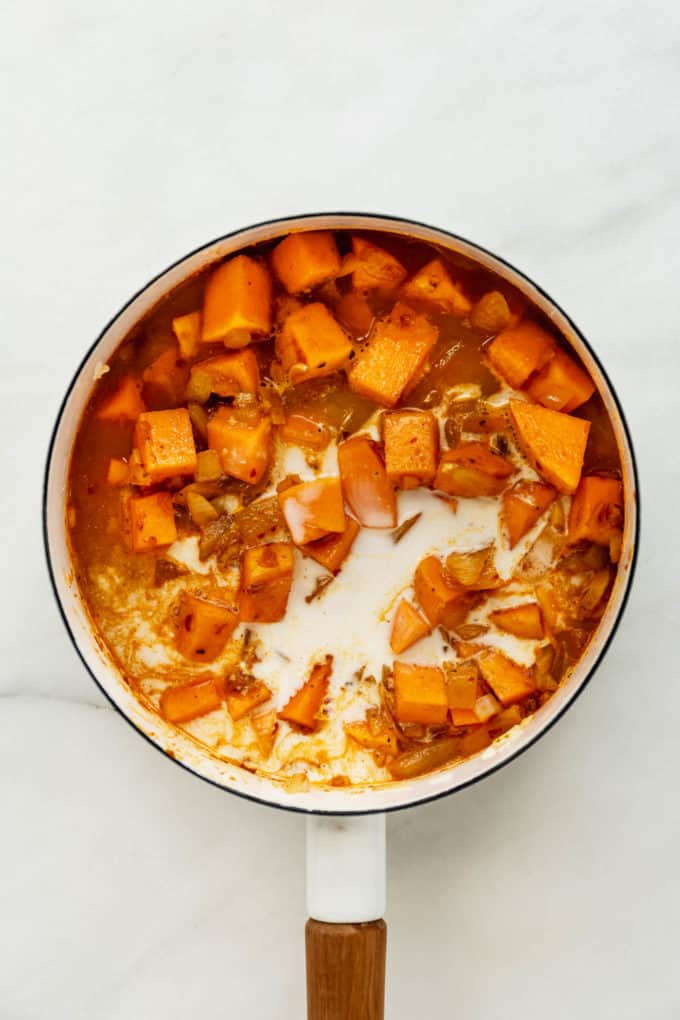 A white pot with squash, broth and coconut milk in it