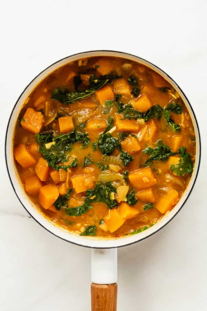 a white pot with butternut squash and kale curry in it