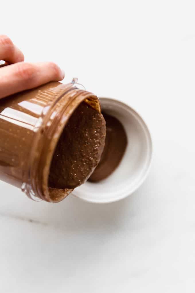a hand pouring blended baked oats into a ramekin