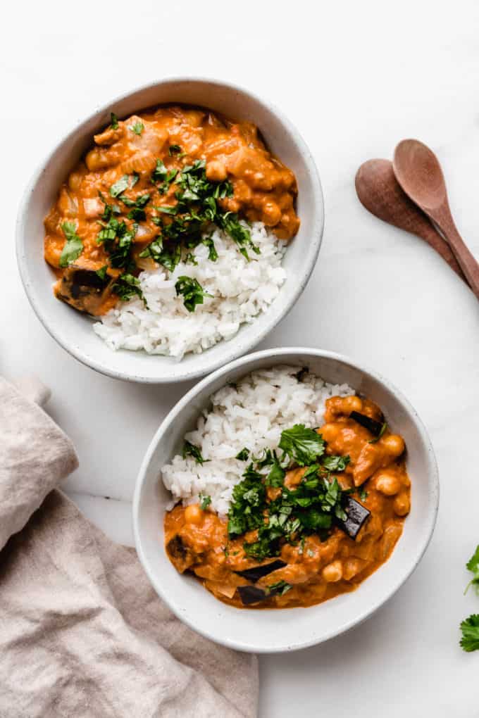 two bowls of eggplant curry and rice topped with chopped cilantro