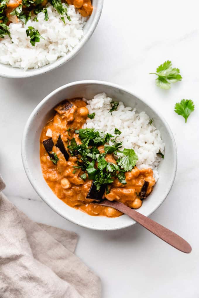 A bowl of eggplant curry with rice topped with cilantro