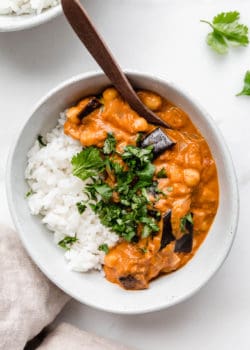 Eggplant curry and rice in a white bowl with a wood spoon