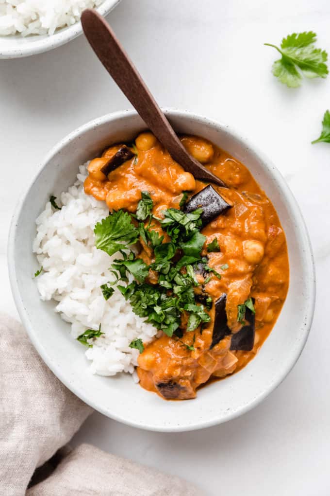 Eggplant curry and rice in a white bowl with a wood spoon