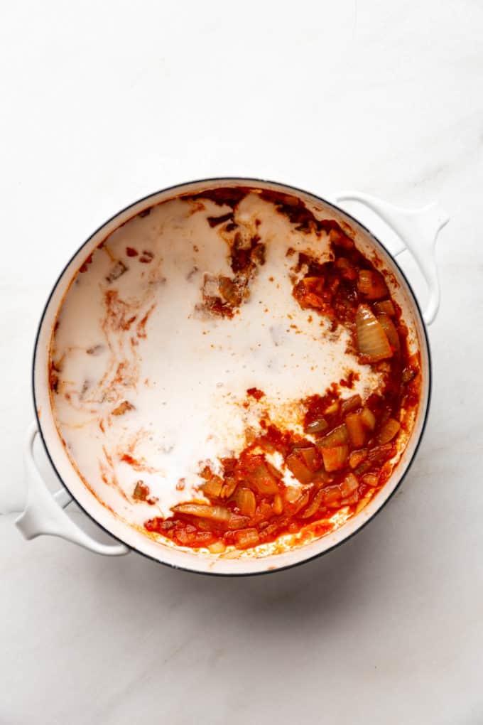 A white pot with coconut milk and tomato sauce in it
