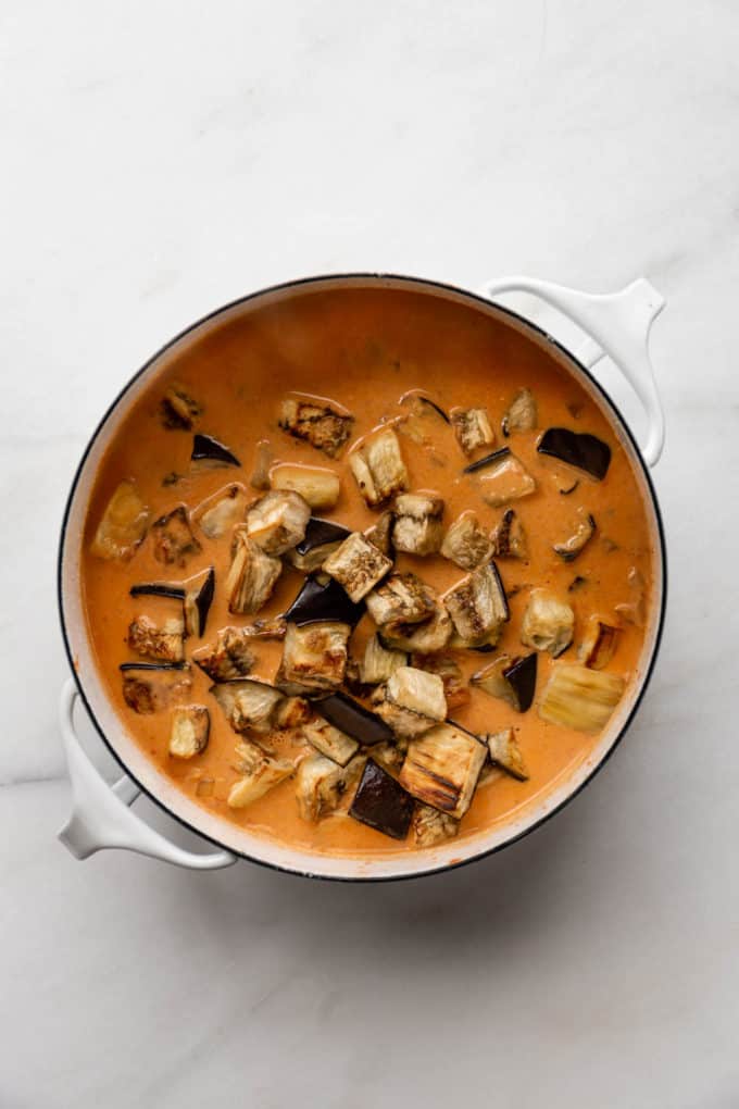 A white pot with curry sauce and cubes of eggplant in it