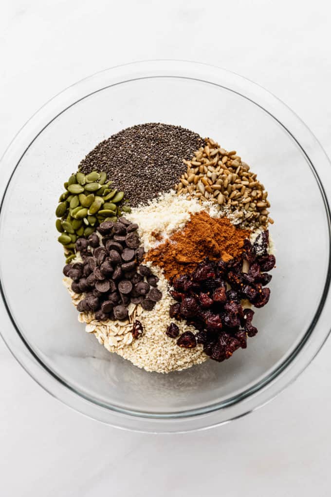 a mixing bowl with oats, nuts, seeds, cranberries and chocolate chips in it