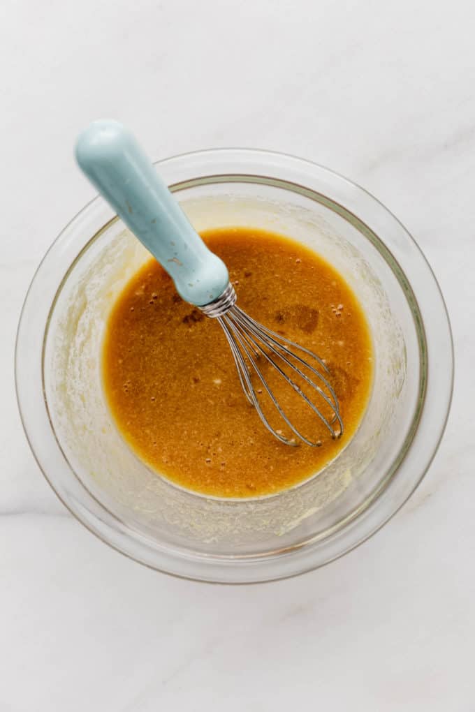a clear mixing bowl with wet ingredients for cookies and a whisk