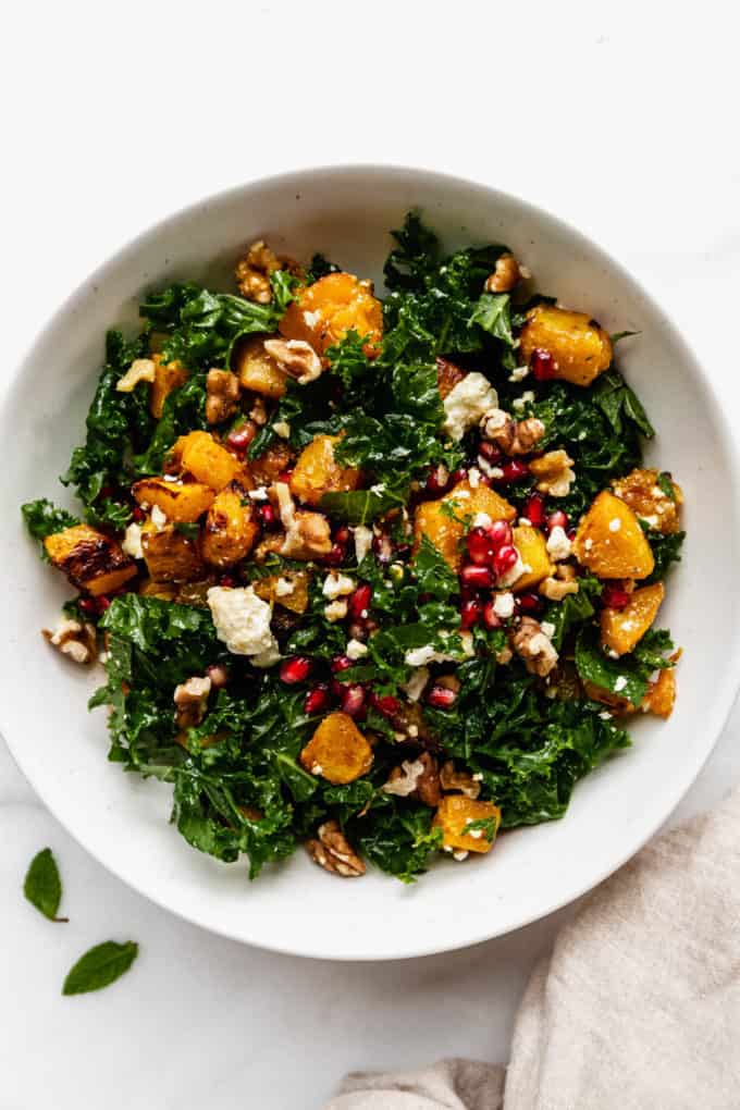 A white bowl with roasted pumpkin salad in it and a beige napkin on the side