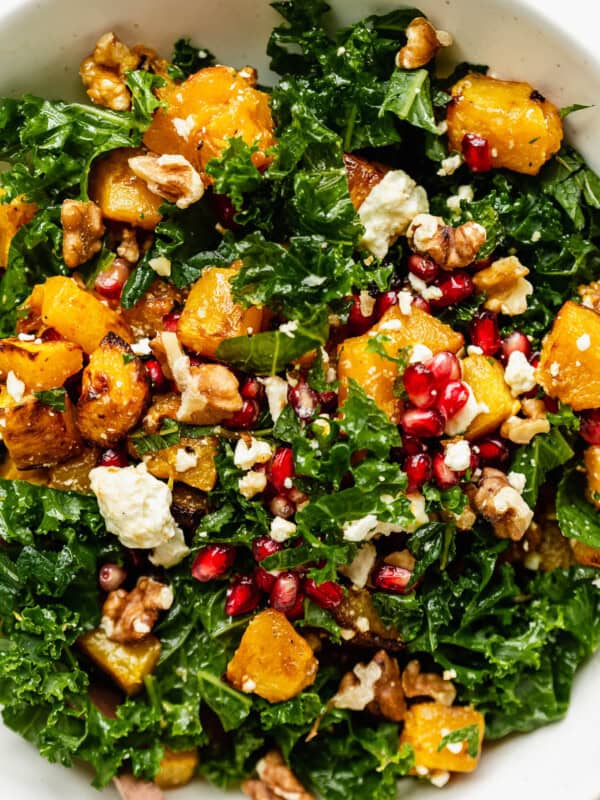A close up of a kale and pumpkin salad topped with walnuts and pomegranate