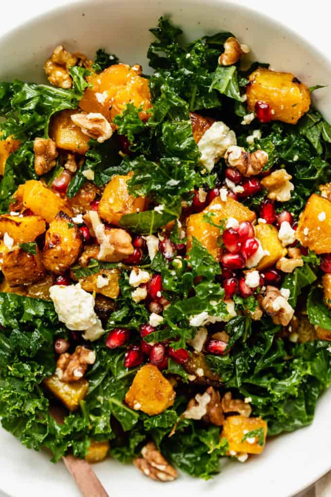 A close up of a kale and pumpkin salad topped with walnuts and pomegranate
