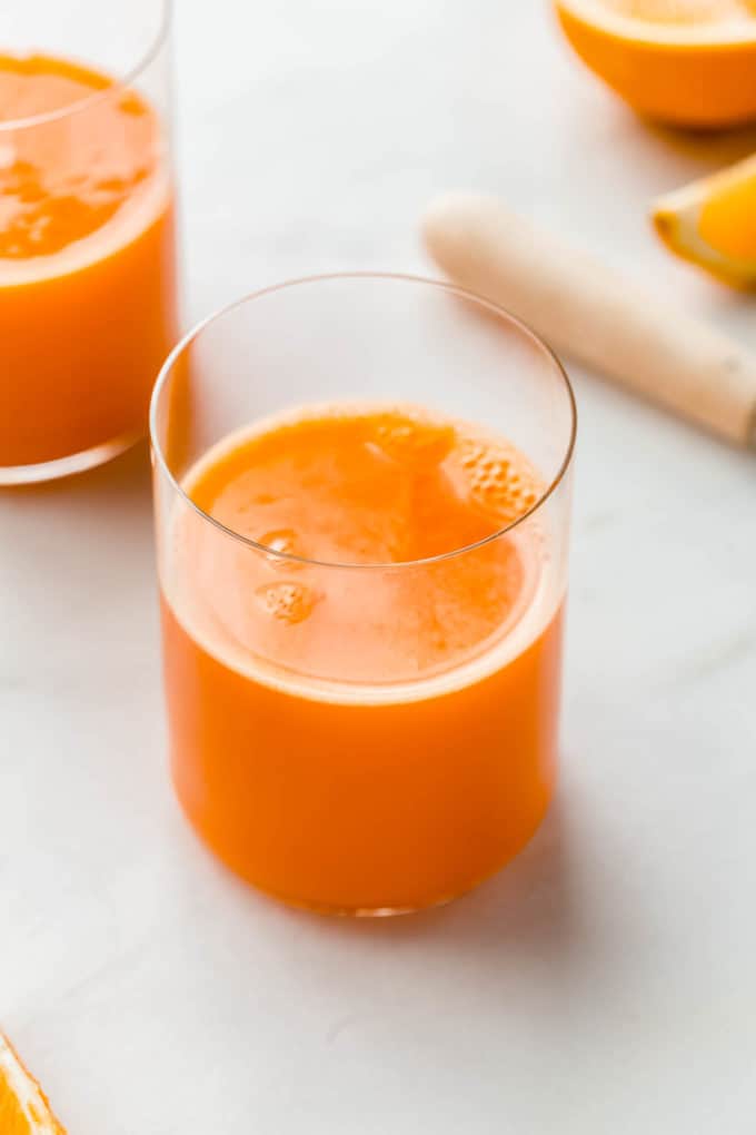 A cup of immune boosting orange and carrot juice with oranges in the background
