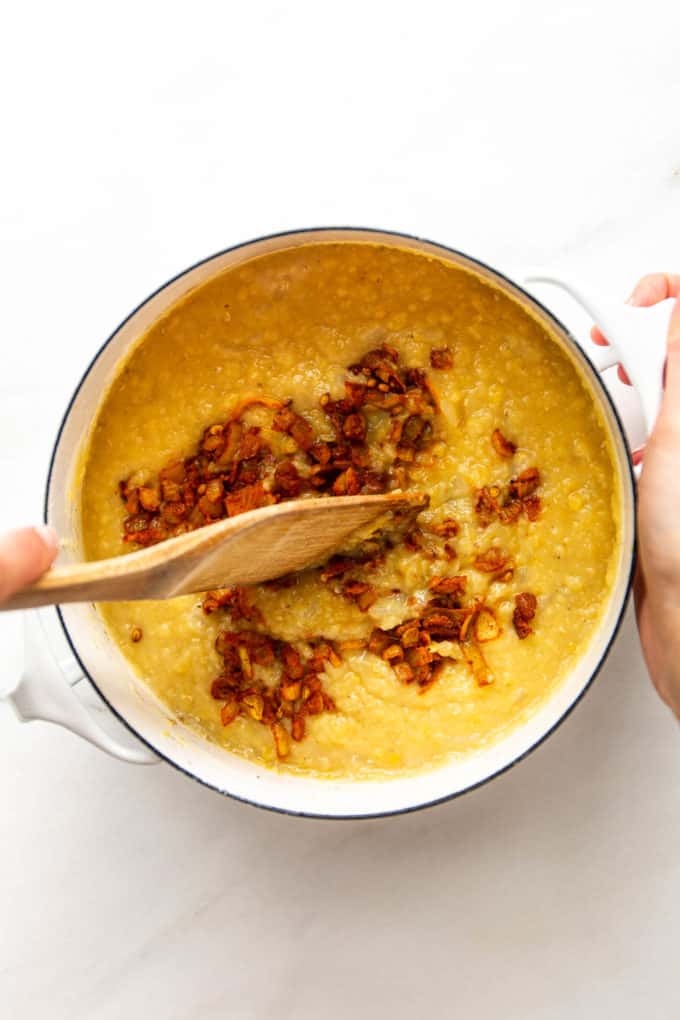 Lentil dahl in a white pot with onions being mixed into it