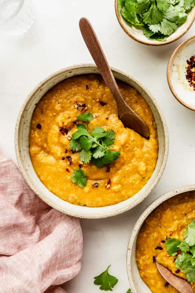 A bowl of red lentil dahl topped with cilantro and a pink napkin on the side