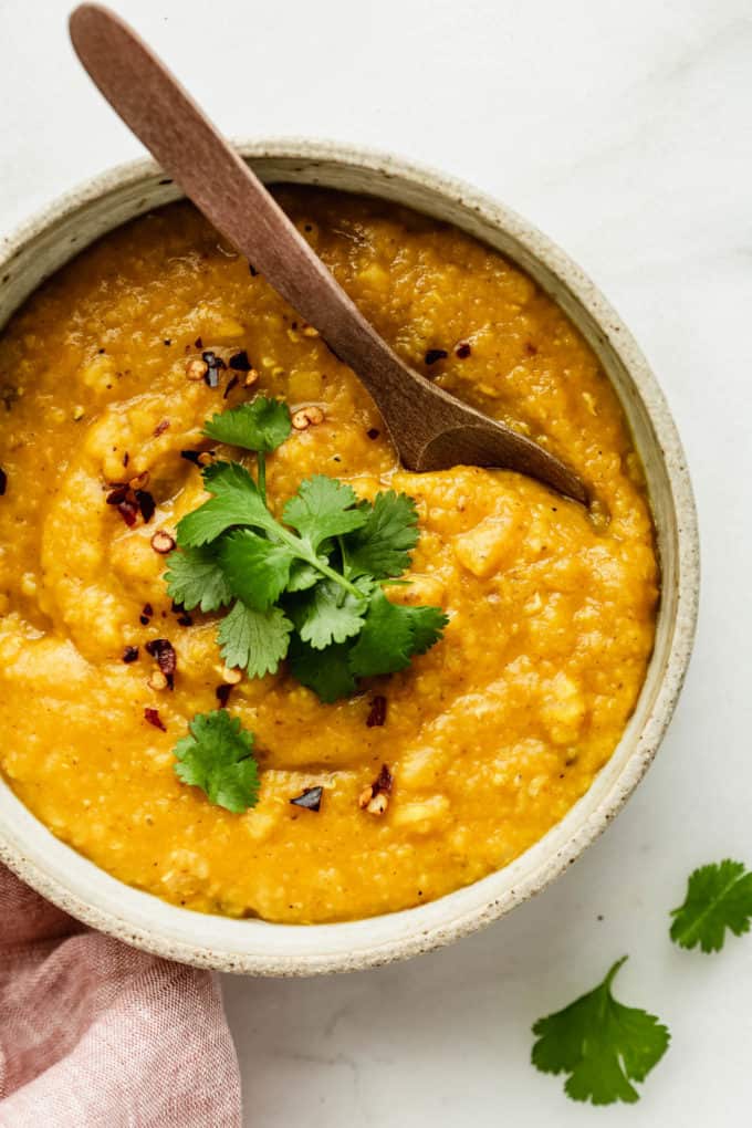 A bowl of lentil dahl with a wood spoon in it