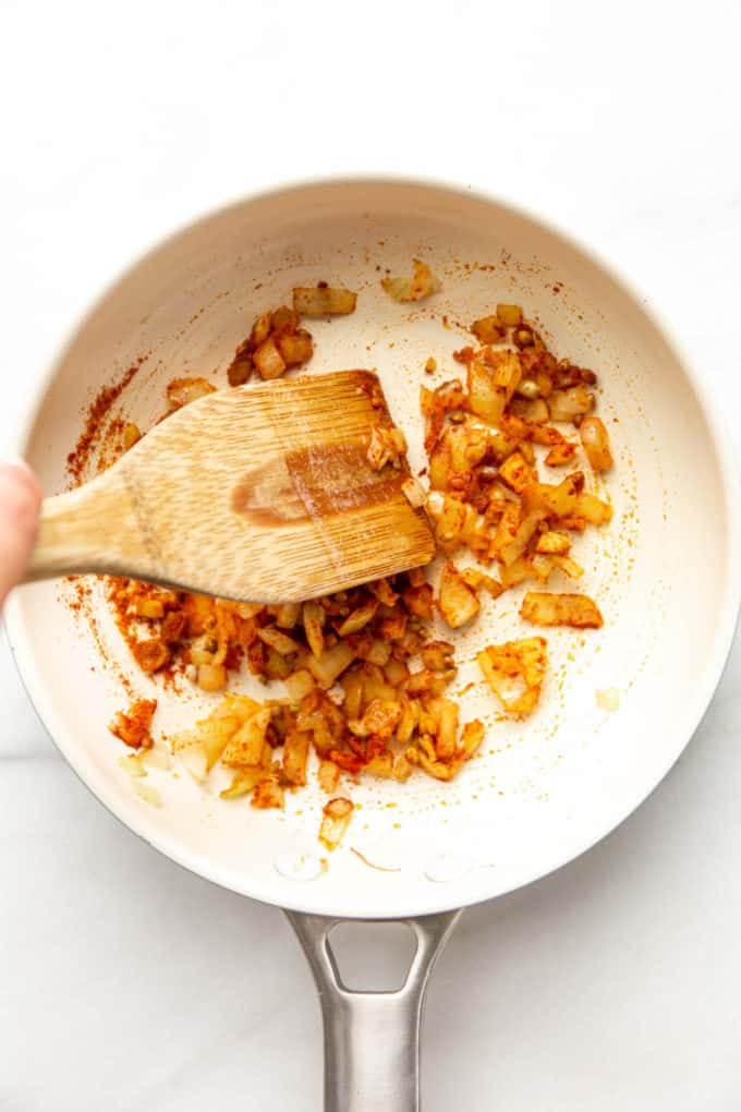 A white pan with onions and spices in it mixed together