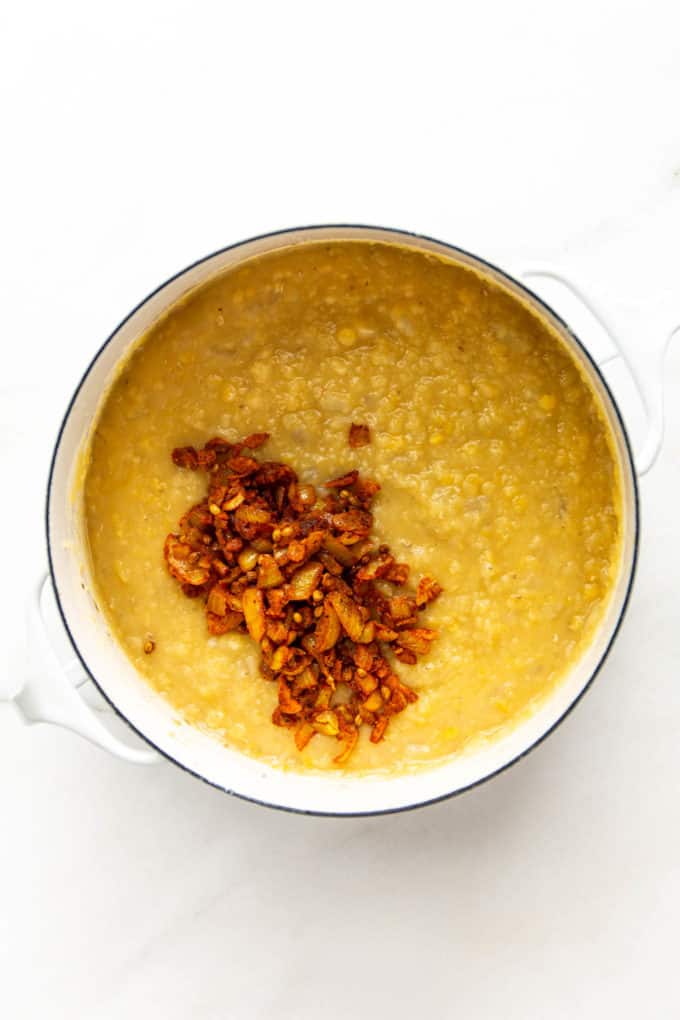 A white pot with lentil dahl, onions and spices in it