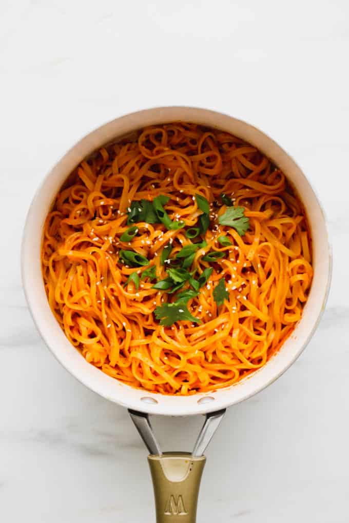 Thai Red Curry Noodles topped with scallions and cilantro in a white pot