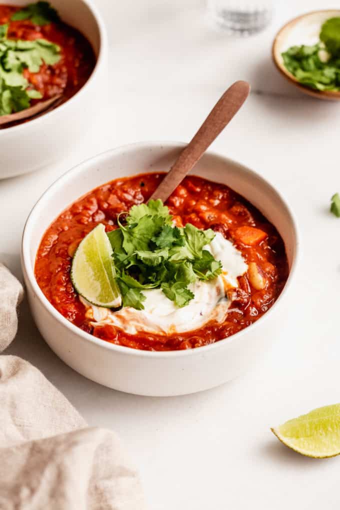 A bowl of white chili on a table with lime and a napkin on the side