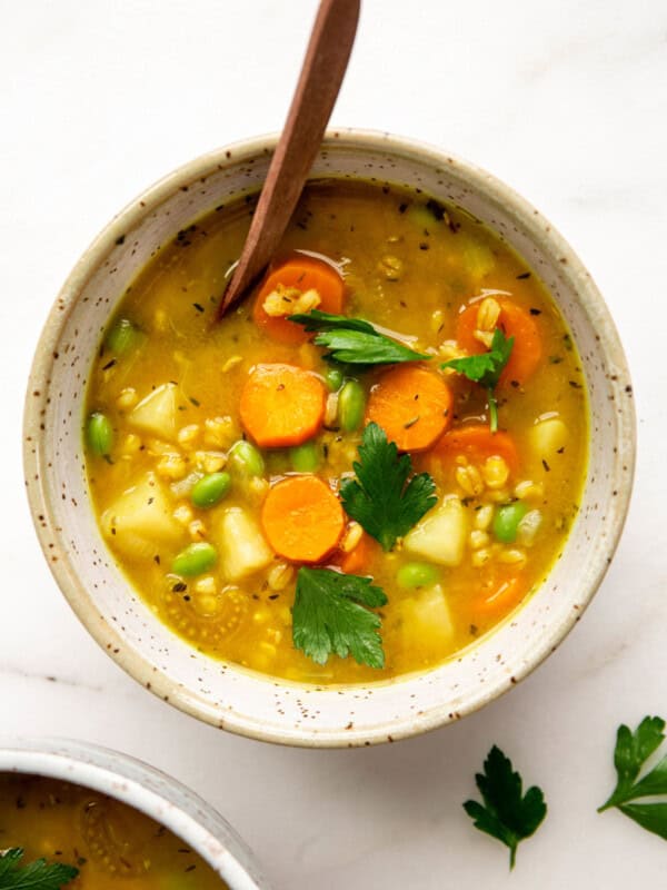 vegetable barley soup in a speckled bowl with a wood spoon