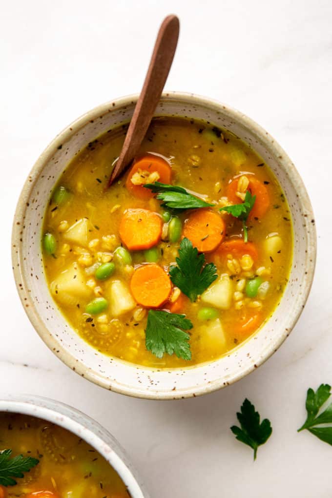 vegetable barley soup in a speckled bowl with a wood spoon