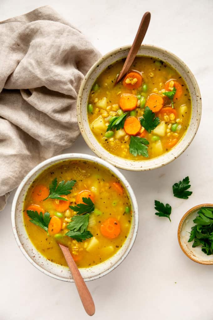 two bowls of vegetable barley soup with a beige napkin on the side