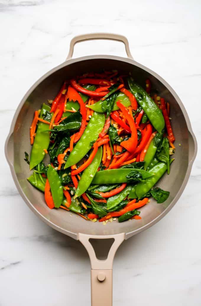 A pan with snow peas, peppers, carrots and spinach in it