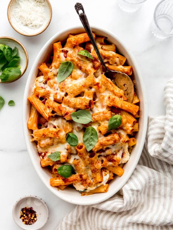 Baked ziti in an oval dish with a striped napkin on the side