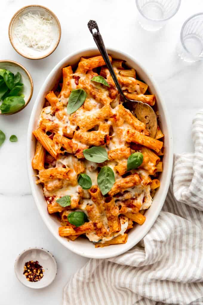 Baked ziti in an oval dish with a striped napkin on the side