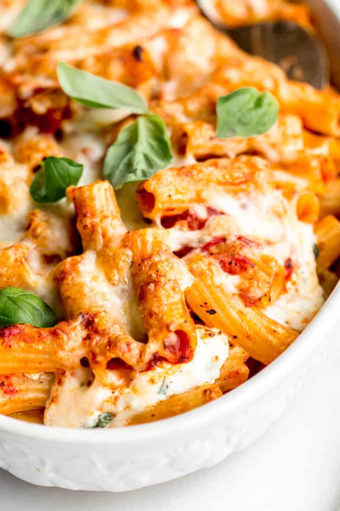 A close up of baked ziti topped with cheese and basil leaves