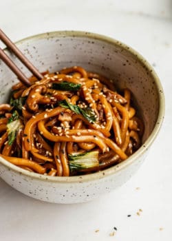 Yaki udon in a speckled ceramic bowl with wood chopsticks in it
