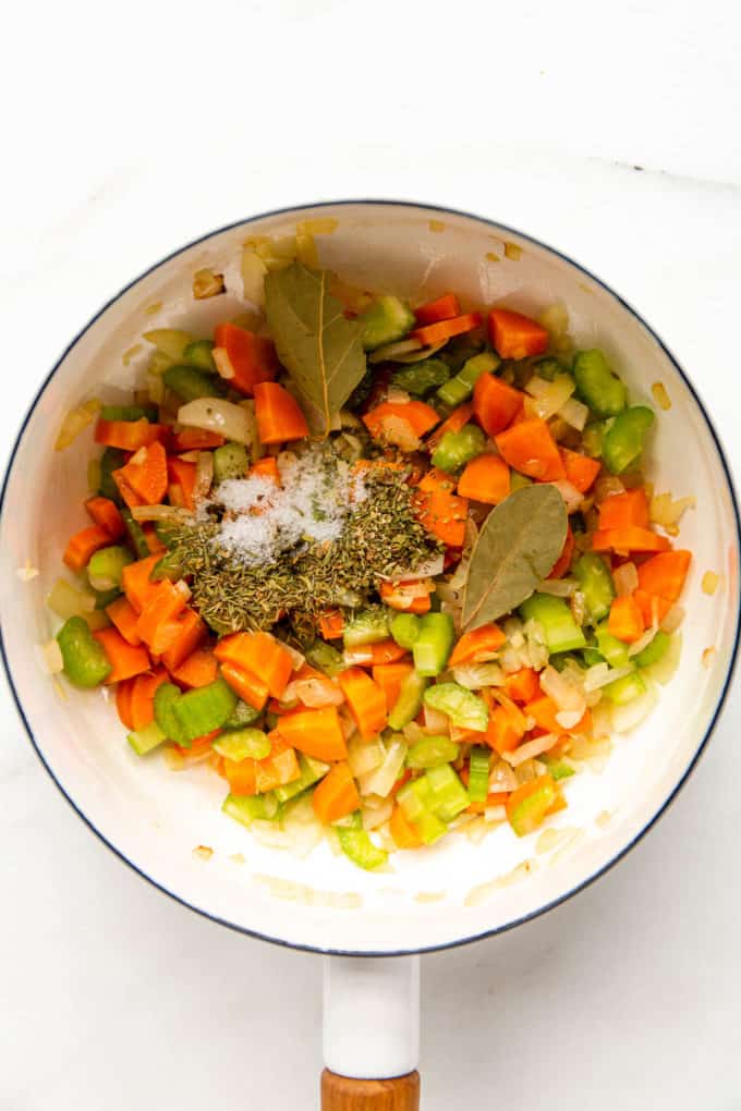 a white pot with vegetables, bay leaves and dried herbs in it