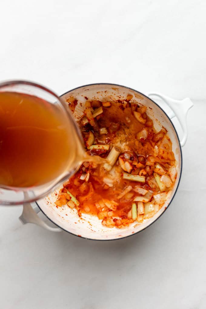 broth being poured into a white pot with onions and lemongrass and curry paste