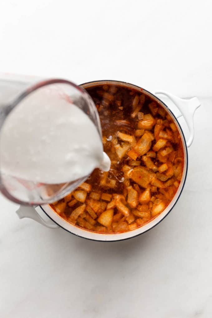 coconut milk being poured into a pot of soup