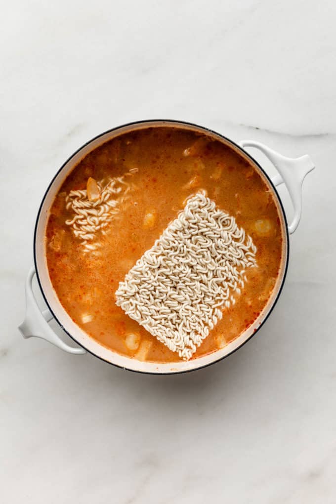 A pot of coconut curry soup with ramen noodles in it